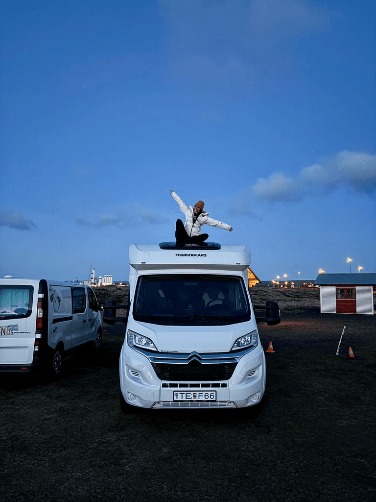 Traveller sitting on top of a campervan at twilight